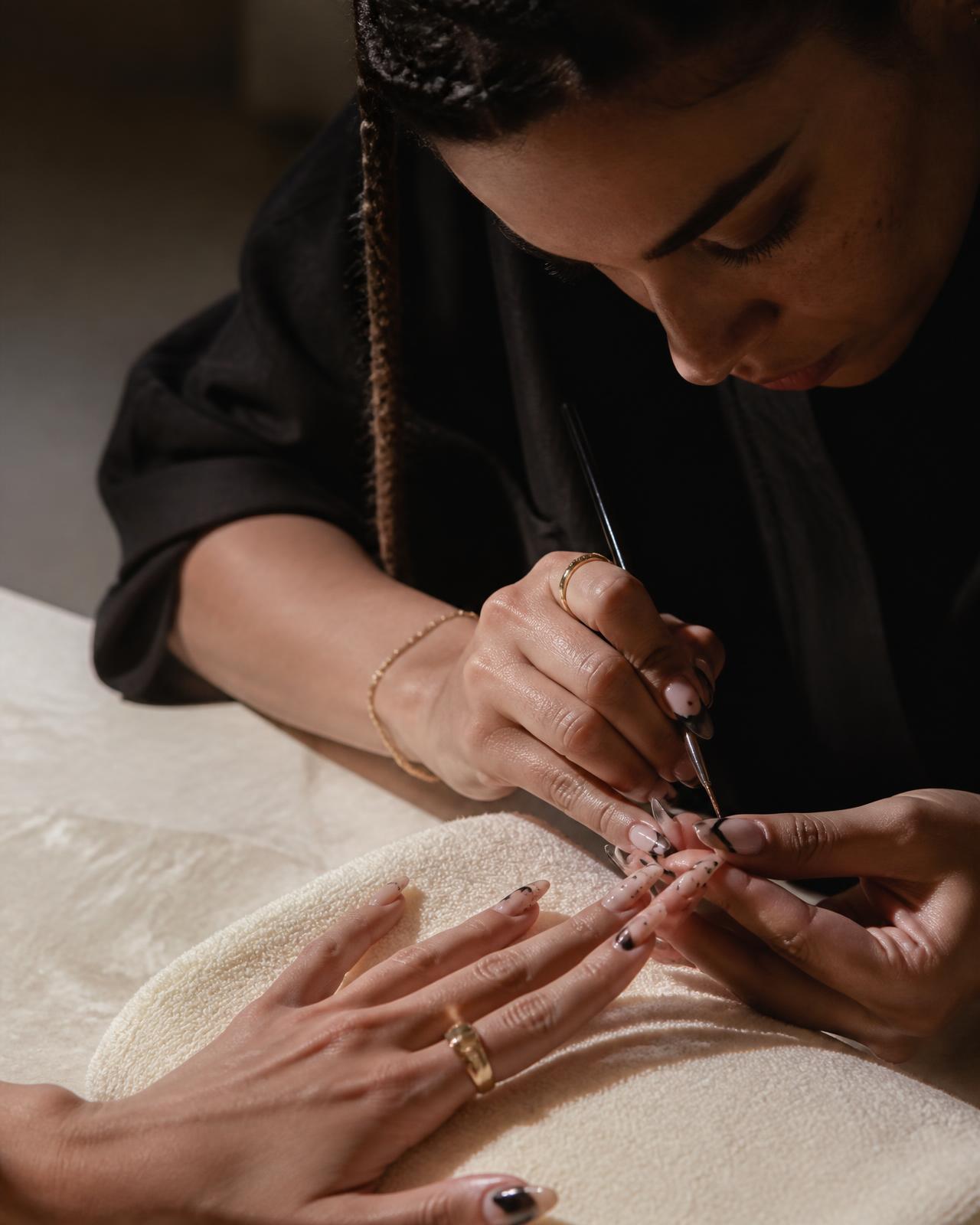 A nail artist painting a detailed set for a returning client, her previous designs remembered in Clientelle.